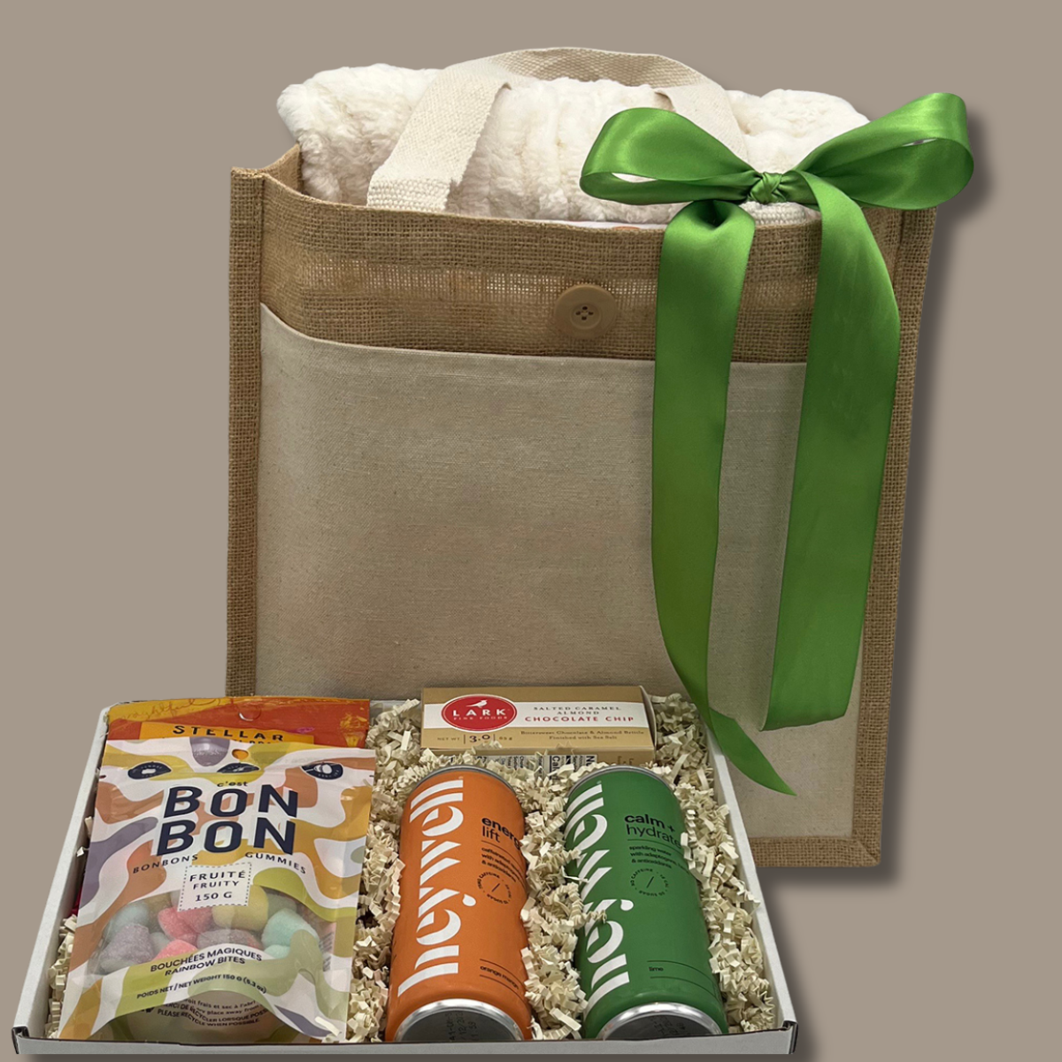 Gift bag with a green ribbon and a box of snacks on a beige background