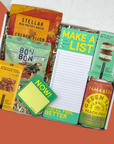 Assorted snacks and a notepad in a box with a colorful design.