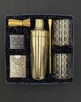 Five O’Clock Gift Box with gold cocktail shaker, lowball glasses, jigger, bar spoon, playing cards, and chocolate caramels