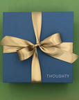 Blue gift box with a gold ribbon on a green background, featuring the brand 'THOUGHTY'.