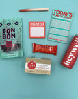 Flat lay of High Five Kit contents including Larabar, raspberry gummies, gradient pen, and sparkling energy drink