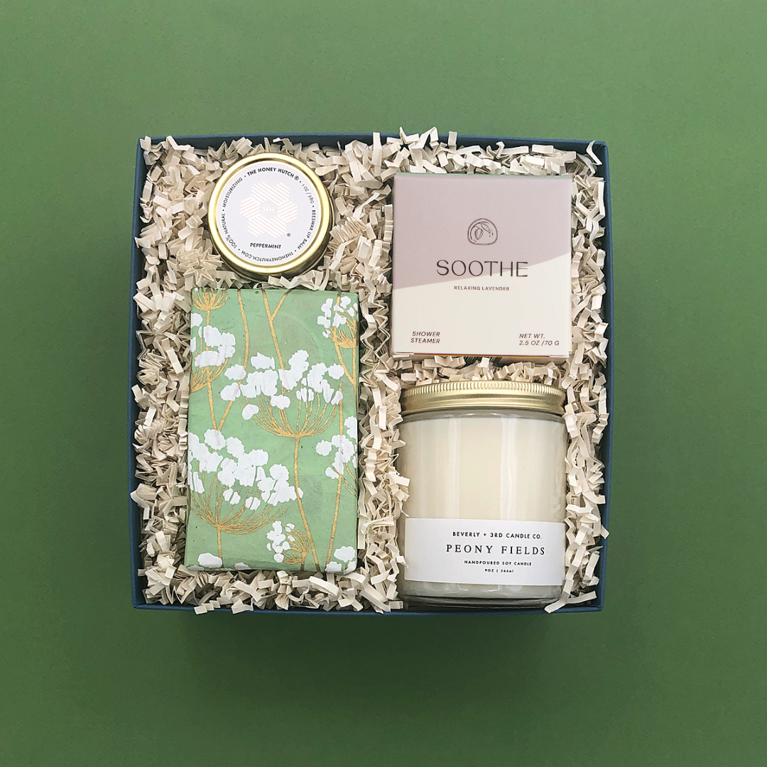 Self-care gift box featuring relaxing candle, shower steamer, nourishing lip balm, and gourmet cookies