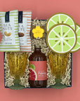 Gift set with Paloma bottle, lime-themed glasses, and sea nut snacks on a pink background