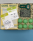 Box containing college game night items including dice, score pads, and green balls on a blue background
