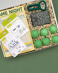 Box of college party supplies including cards, dice, and green balls on a blue background