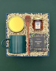 Gift set with a mug, jar, wooden spoon, and tea box on a green background