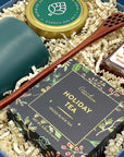 Close up of gift set with holiday tea, honey, balsam candle and green ceramic mug.