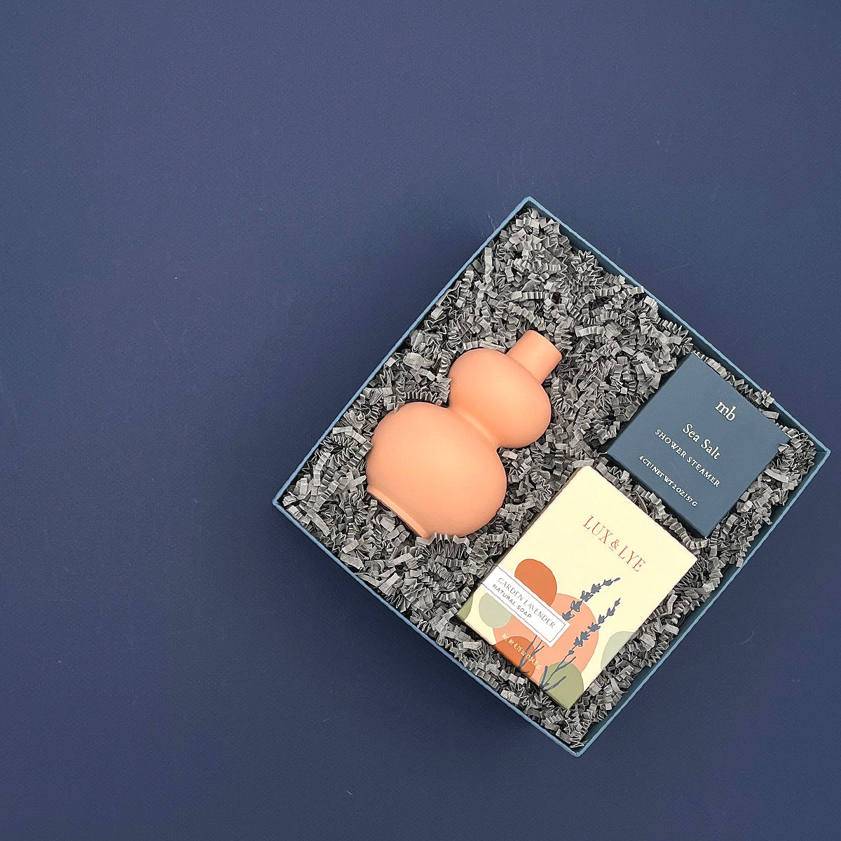 Thoughtful lavender gift with coral vase, botanical soap, and refreshing shower steamer in a blue gift box.
