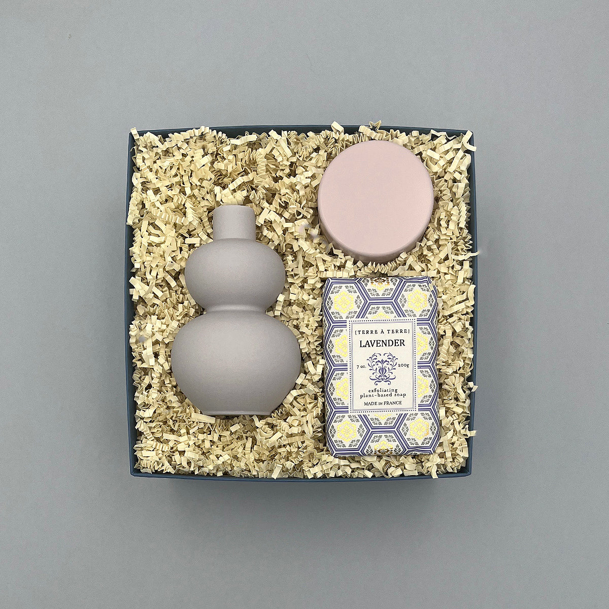 Set of a purple vase, lavender candle, and lavender soap in a box on a gray background