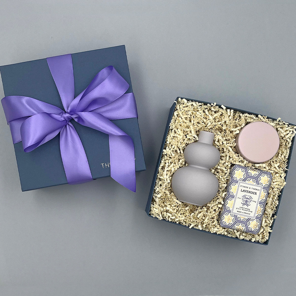 Set of a purple vase, lavender candle, and lavender soap in a box on a gray background