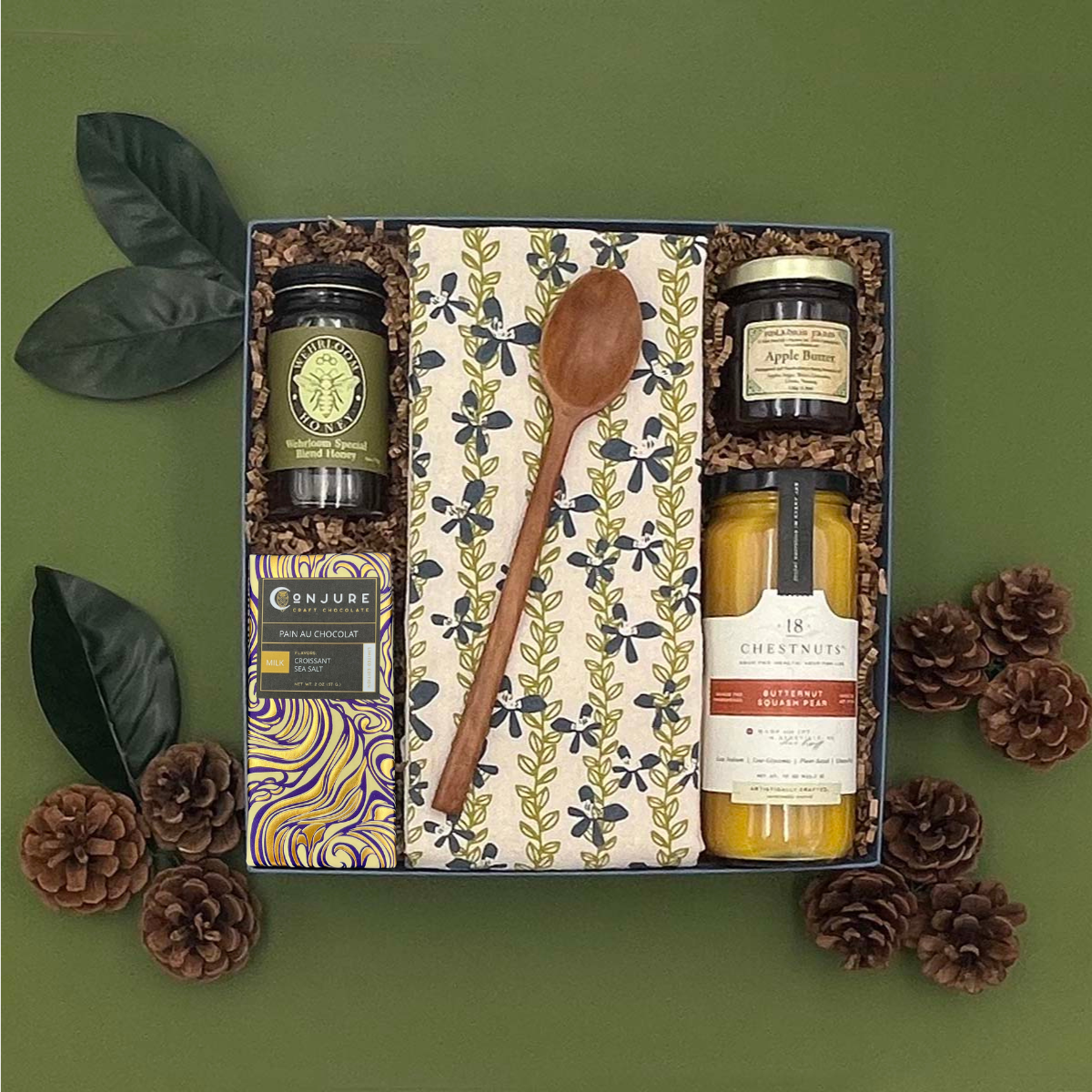 Gift set with jars, a wooden spoon, and a tea towel on a green background
