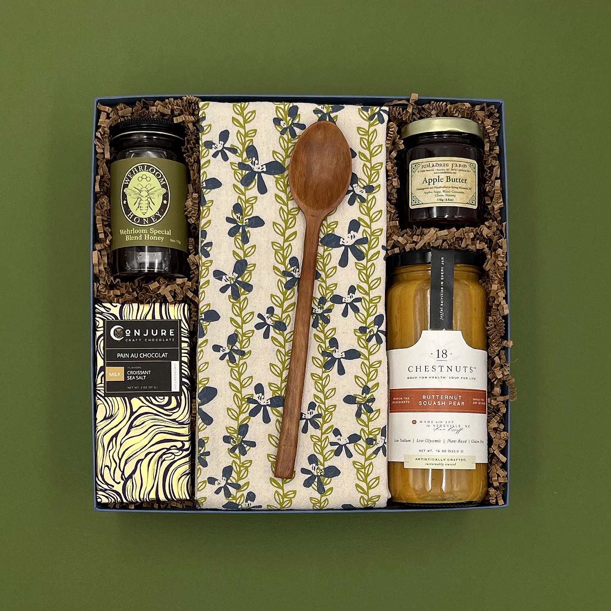 Gift set with a wooden spoon, jars, and a box on a green background
