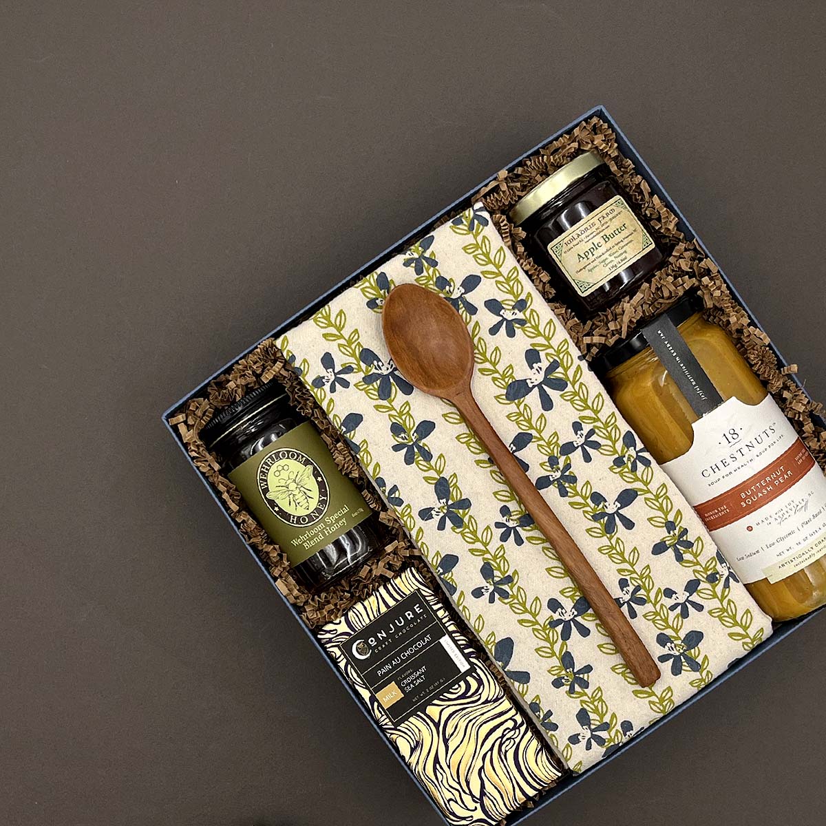 Gift set with jars, a wooden spoon, and a napkin in a decorative box on a dark background
