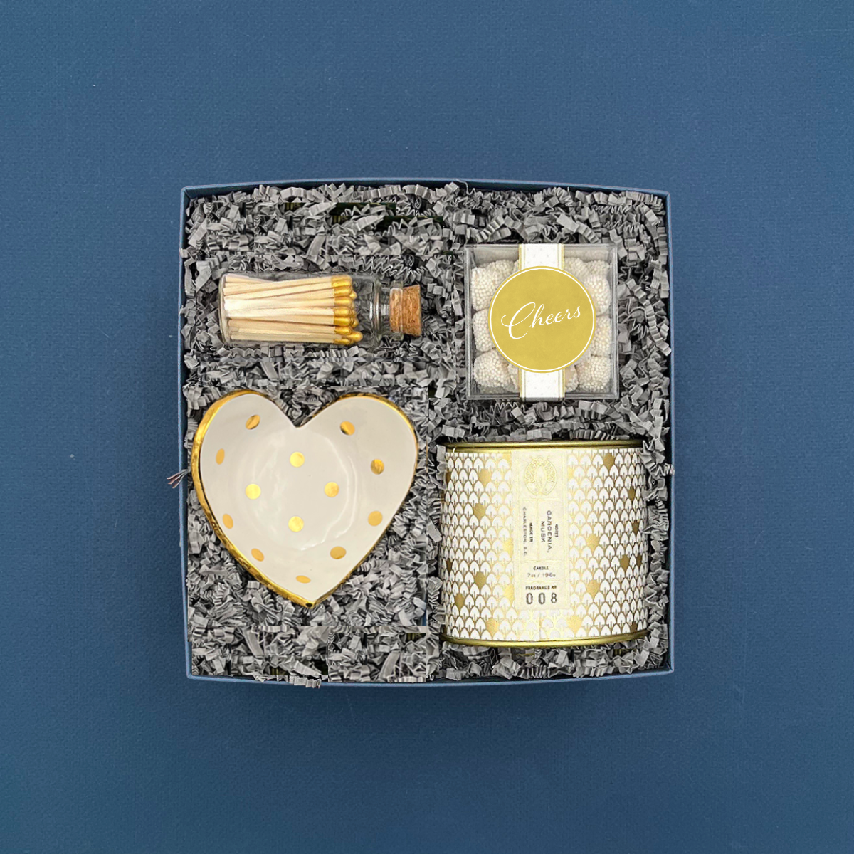 Gift set with candle, heart-shaped dish, matches, and decorative box on a blue background