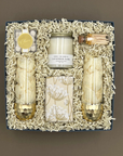 Overhead view of the Cheers to You celebration gift box showing two gold-dipped stemless champagne glasses, Beverly + 3rd Lavender Sage candle, champagne bubble gummies, botanical-wrapped Belgian chocolate chip cookies, and a corked vial of gold-tipped matches in white crinkle paper.