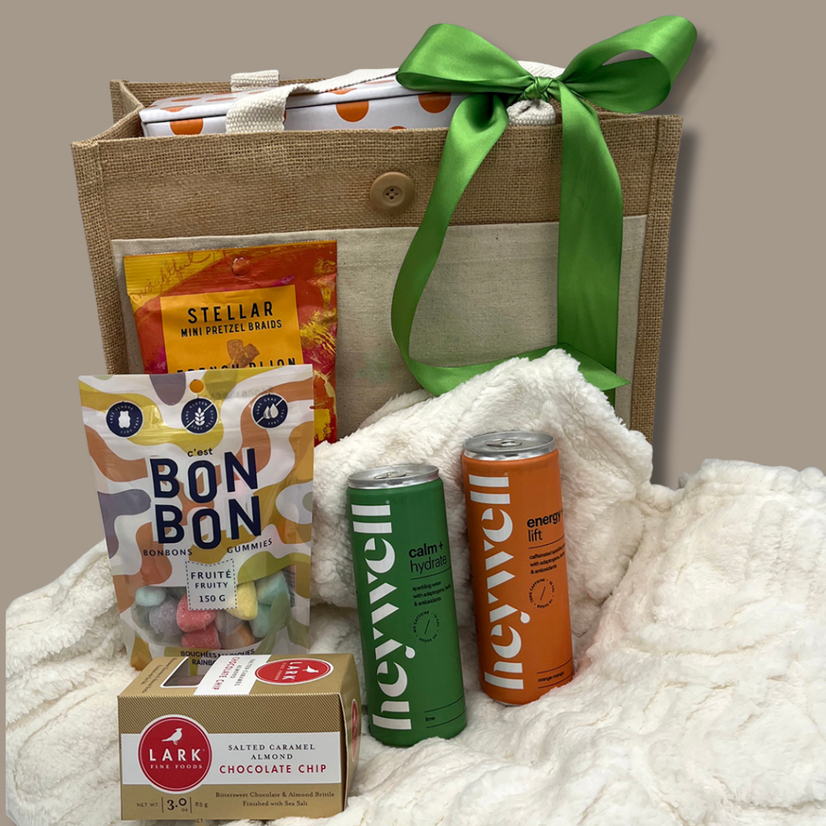 Gift basket with snacks, drinks, and a box on a white blanket