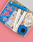 A curated party gift box filled with party supplies, including  a blue portable speaker, disco ball coasters, Pop Rocks candy, and a hangover kit.