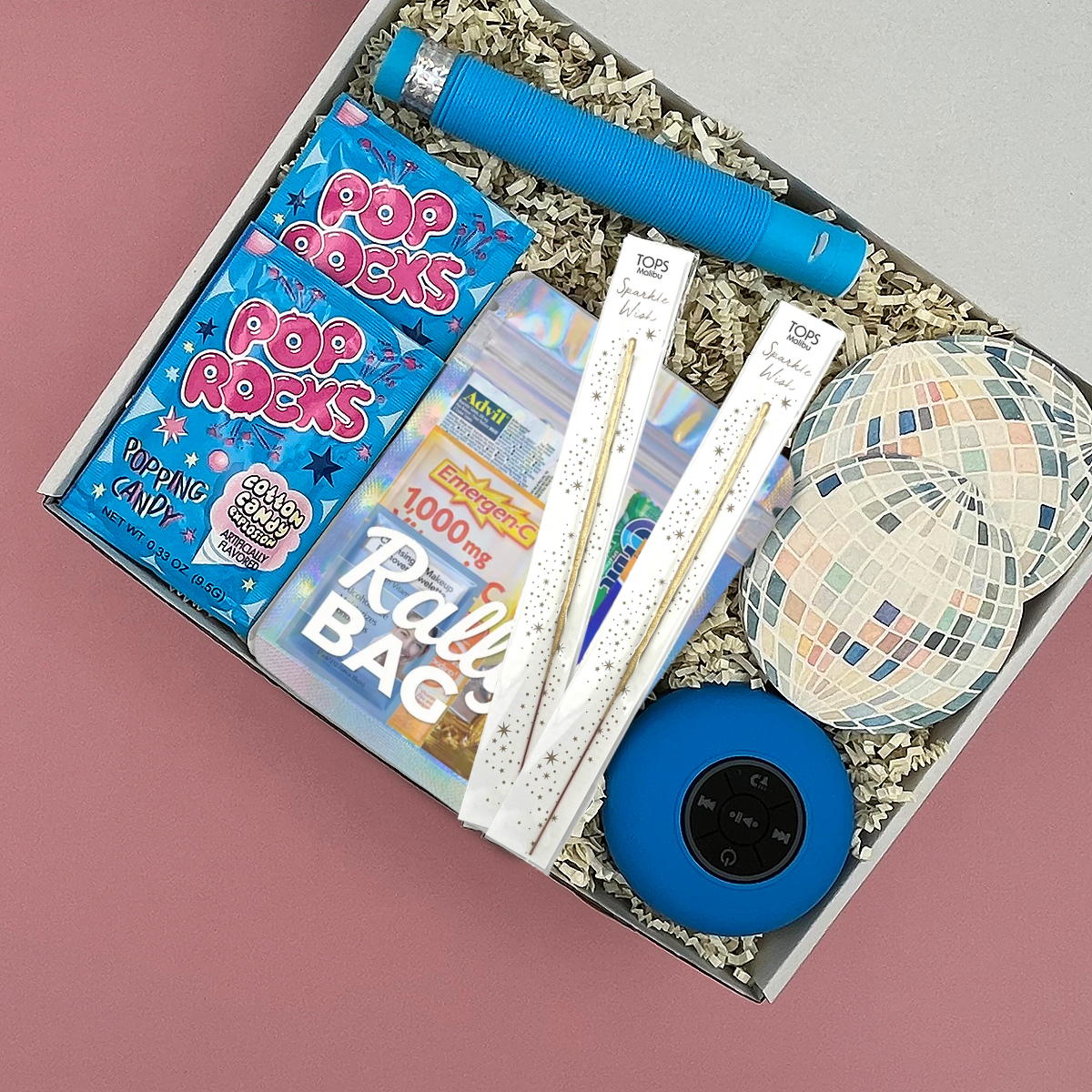 A curated party gift box filled with party supplies, including  a blue portable speaker, disco ball coasters, Pop Rocks candy, and a hangover kit.