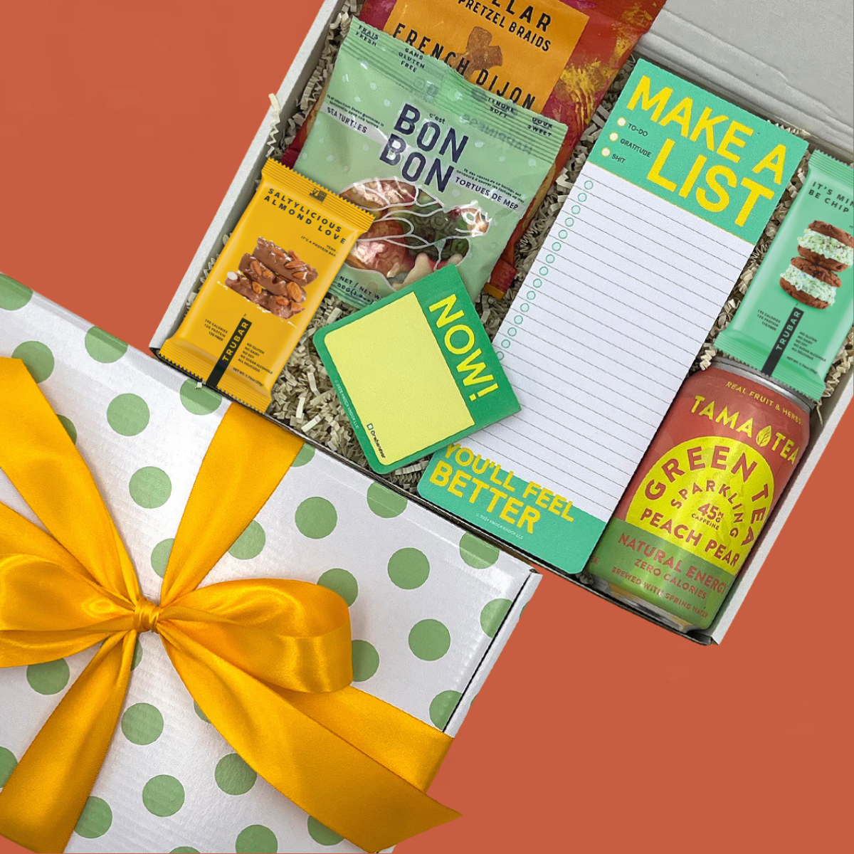 Gift box with snacks, a notepad, and sticky notes on orange background