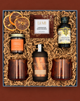 A curated gift box set featuring a bottle of gingerbread syrup, two amber glasses, candle, pecan caramels, a bottle of aromatic bitters, and dried orange slices.