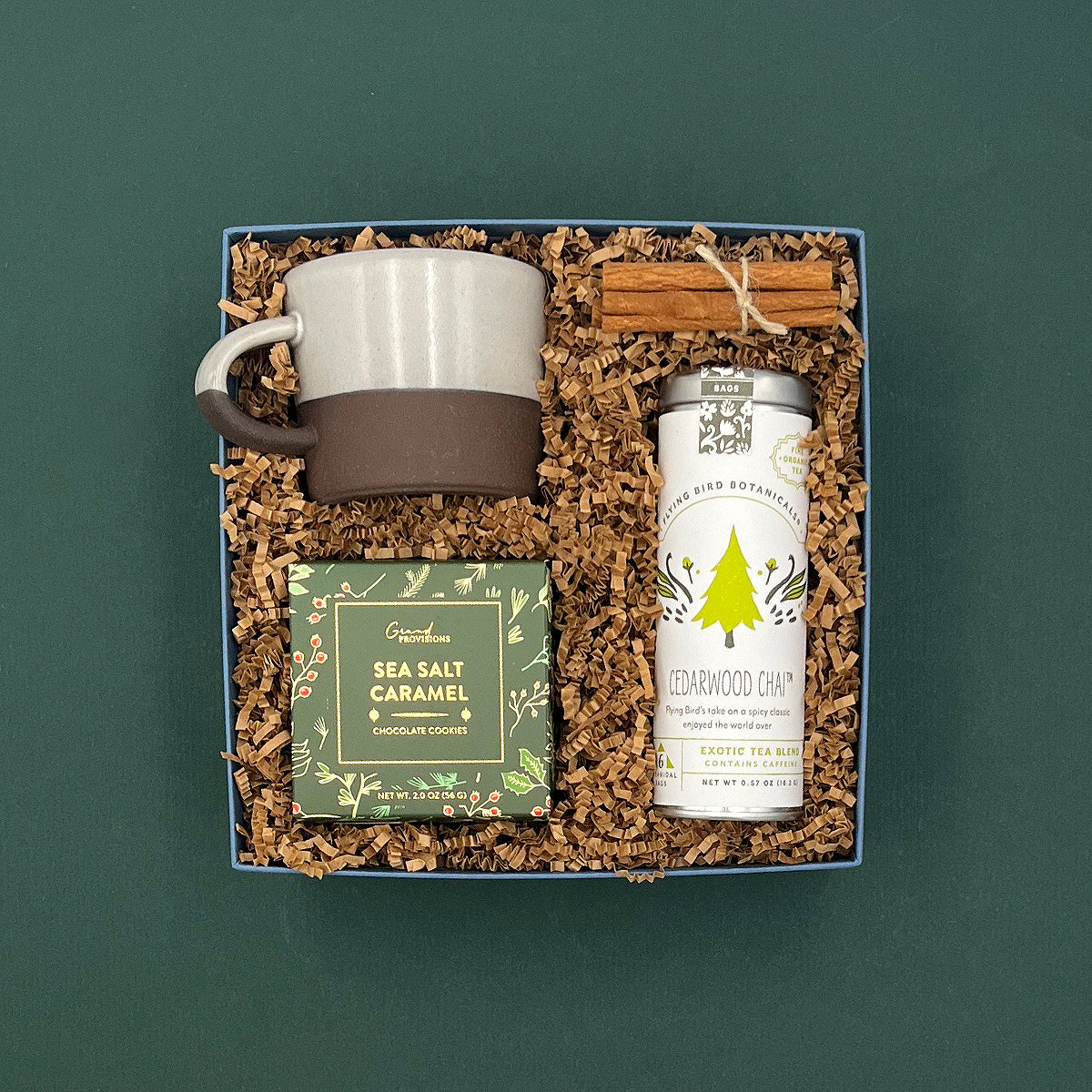 Overhead view of The Fraser Gift Box with chai tea, holiday cookies, ceramic mug, and cinnamon sticks.