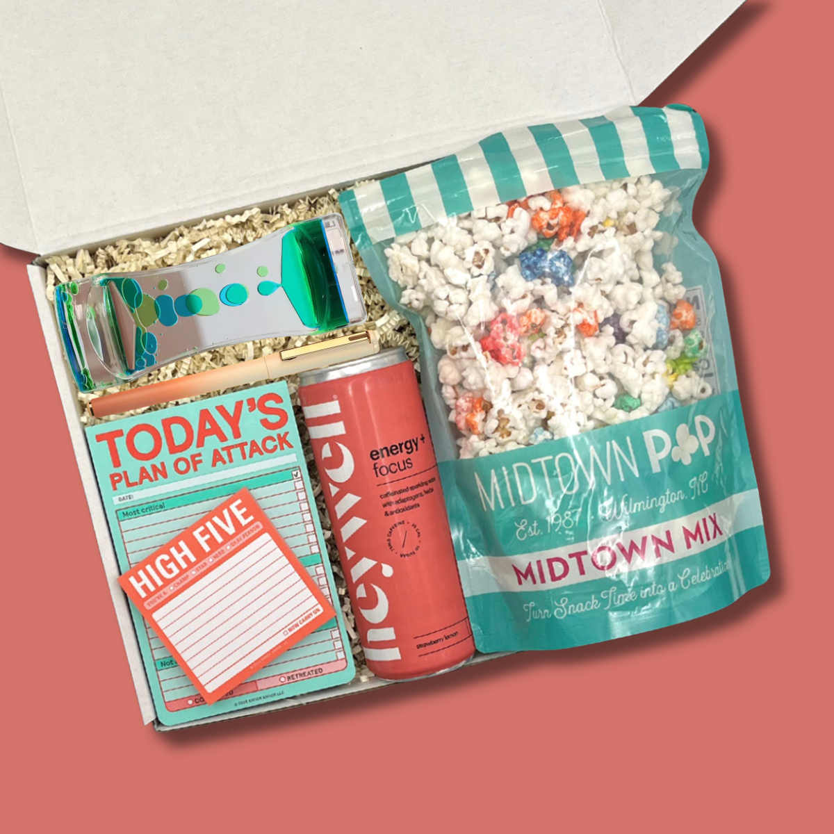 Open gift box with popcorn, energy drink, and planner on a pink background