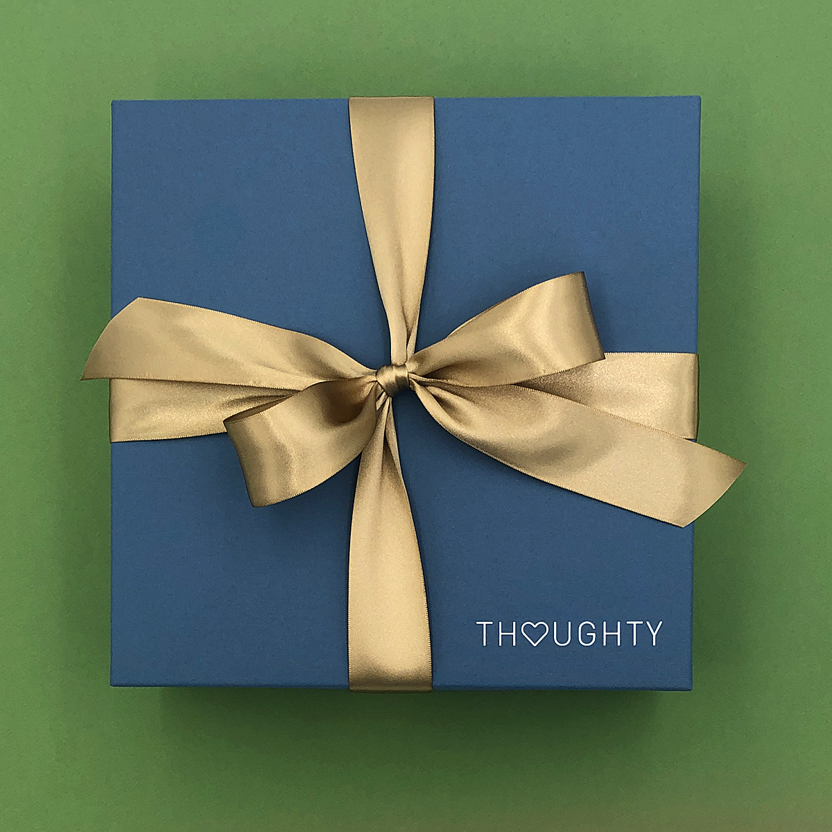 Blue gift box with a gold ribbon on a green background, featuring the brand 'THOUGHTY'.