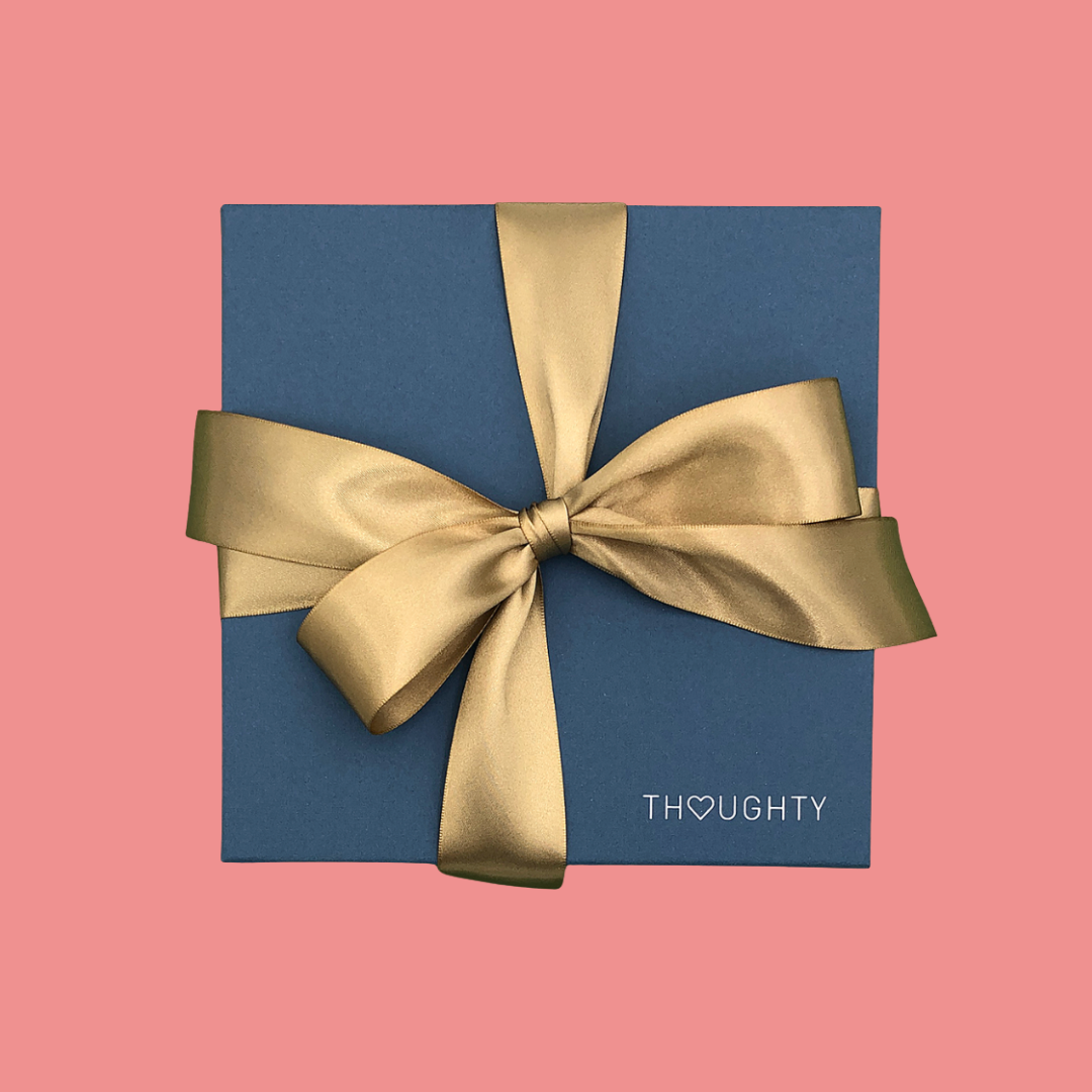 Blue gift box with a gold ribbon on a pink background, featuring the brand 'THOUGHTY'.
