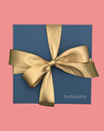 Blue gift box with a gold ribbon on a pink background, featuring the brand 'THOUGHTY'.