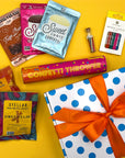 Assorted birthday treats including candy, confetti, and a gift box on a yellow background