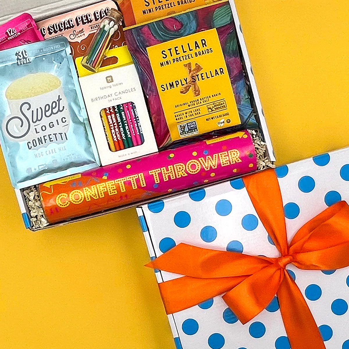 Gift box with confetti-themed items including candles and a 'Simply Stellar' product on a yellow background.