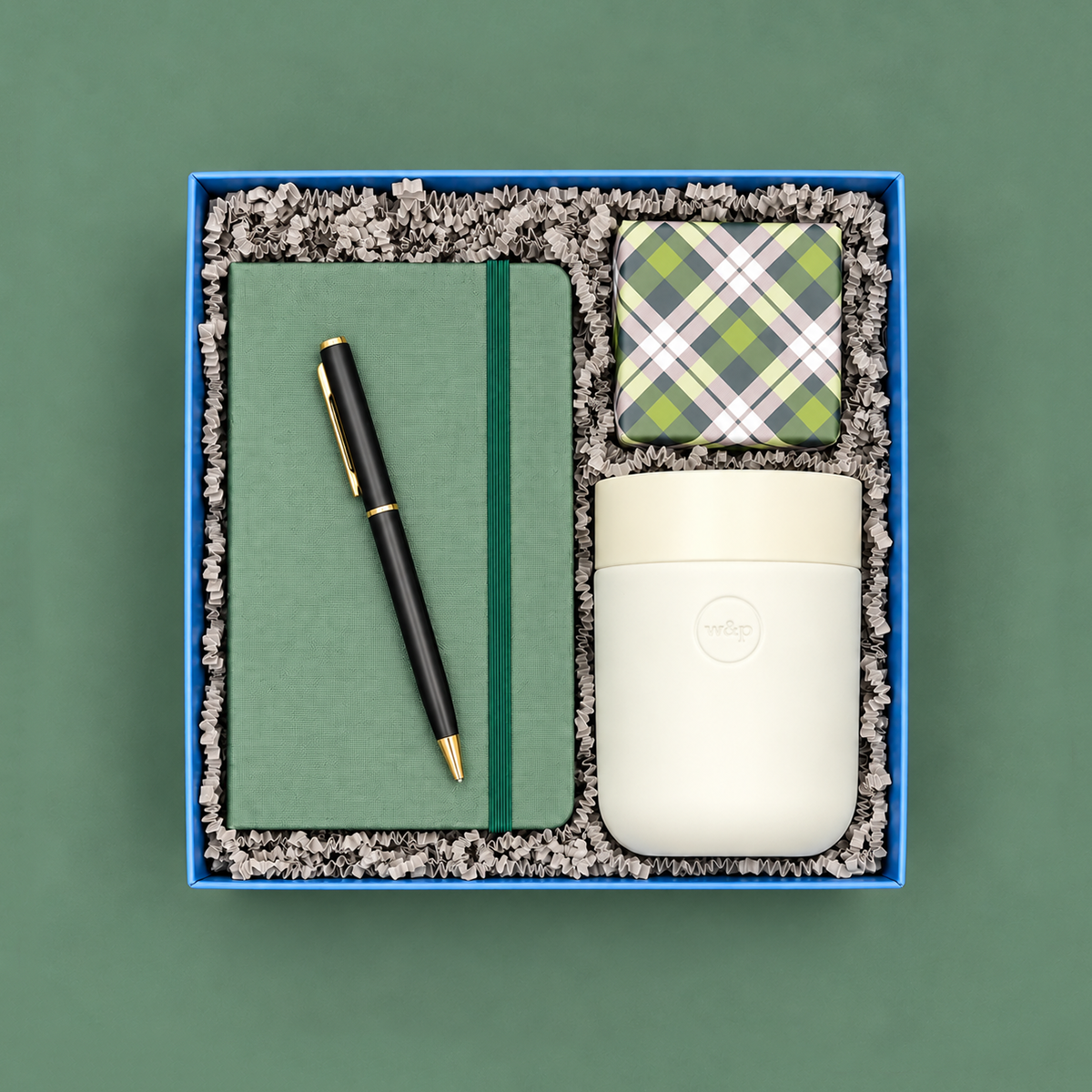 Home Office gift box with green journal, black and gold pen, travel tumbler, and colorful confetti caramels on a green background.