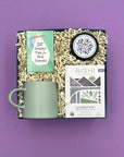 Thoughty Mama to Be baby shower gift box with Rishi Lavender Mint Tea, Thistle Farms body butter, 52 Helpful Tips for New Parents card deck, and a sage green ceramic mug, packed in a navy gift box with cream crinkle paper on a lavender background.