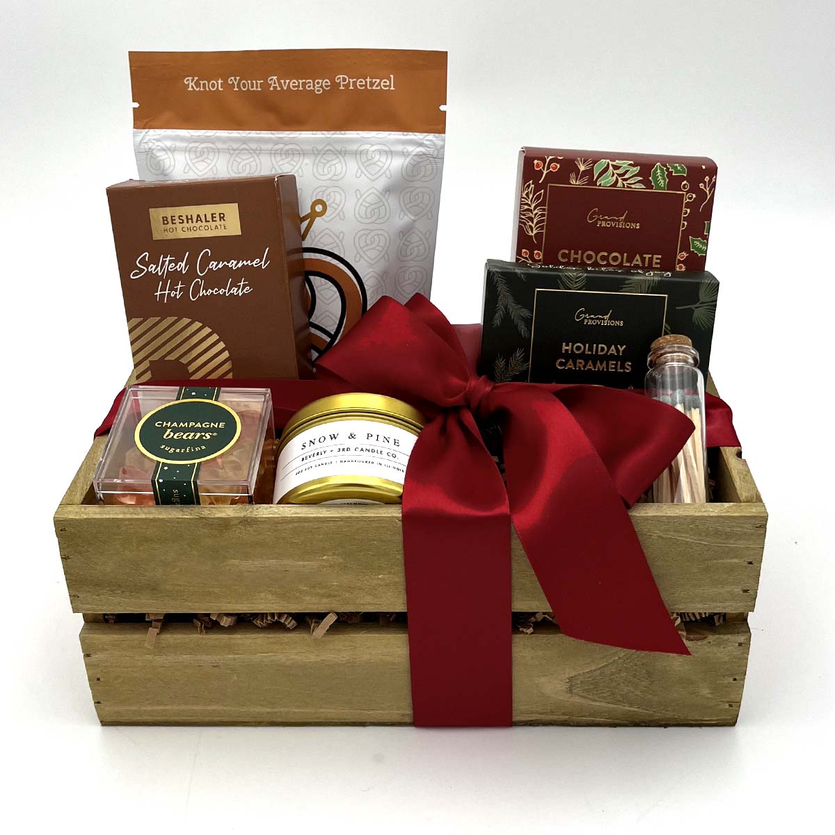 Gift basket with a variety of items including hot chocolate, candy, and a candle, tied with a red ribbon.