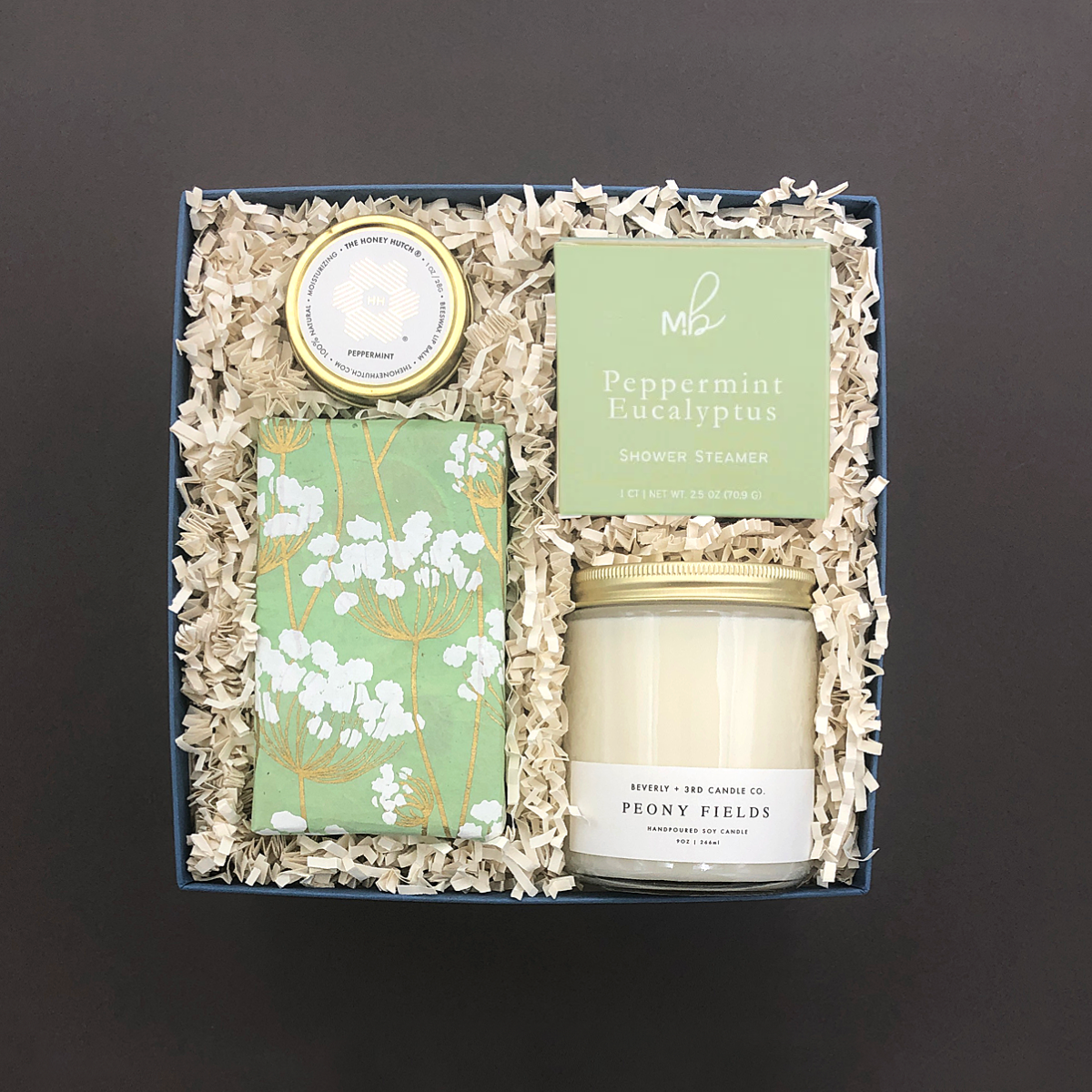 Self-care gift box featuring relaxing candle, shower steamer, nourishing lip balm, and gourmet cookies.