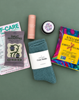 Flat lay of Mood Boost Kit contents including granola, pretzel braids, self care notepad, and cozy cloud socks.
