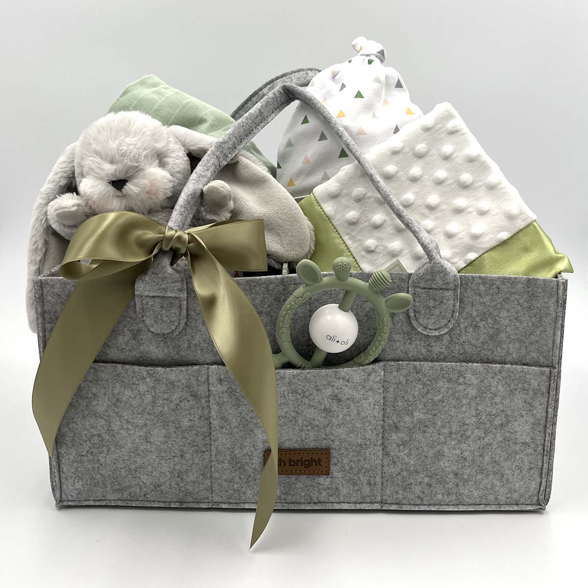 Baby shower gift featuring newborn essentials: blanket, lovie, stuffed bunny, and baby hat in an organized diaper caddy