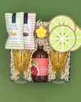 Gift set with Paloma bottle, glasses, and snacks on a green background