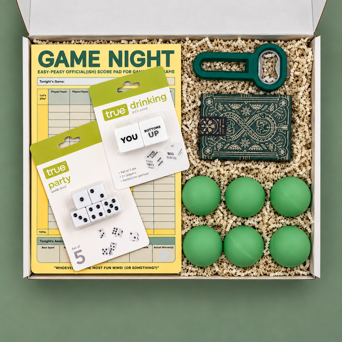 Box containing college game night items including dice, score pads, and green balls on a green background