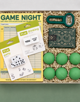 Box containing college game night items including dice, score pads, and green balls on a green background