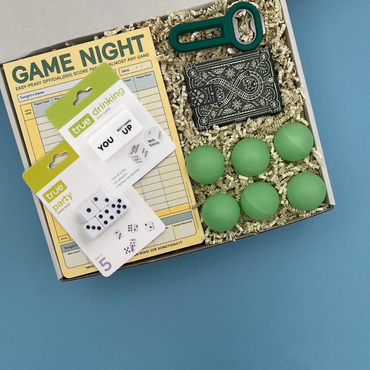 Box of college party supplies including cards, dice, and green balls on a blue background