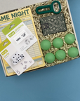 Box of college party supplies including cards, dice, and green balls on a blue background