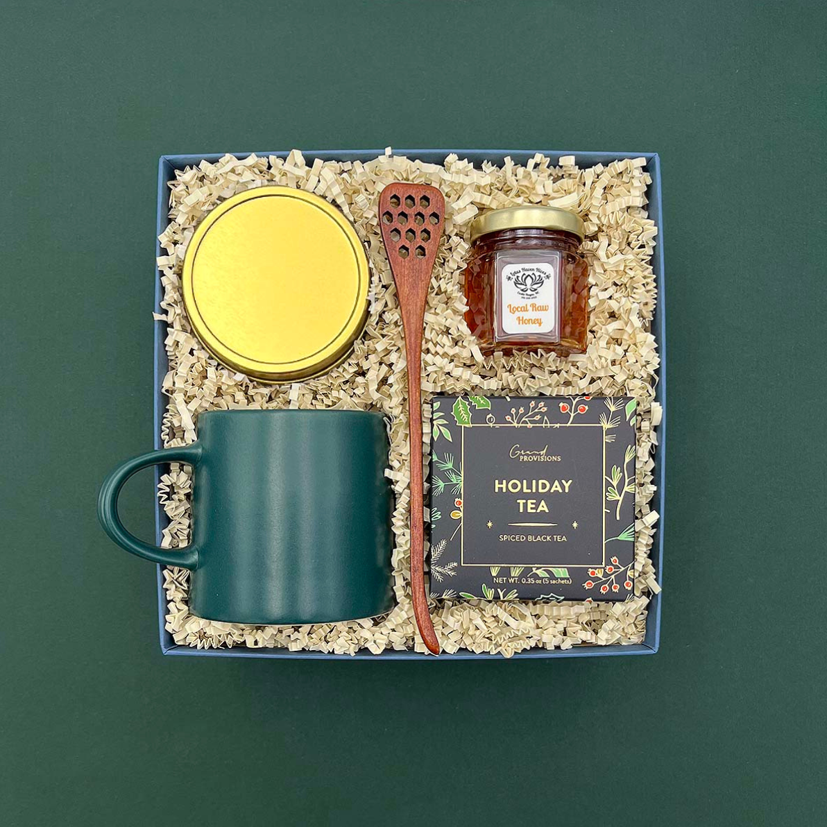 Gift set with a mug, jar, wooden spoon, and tea box on a green background