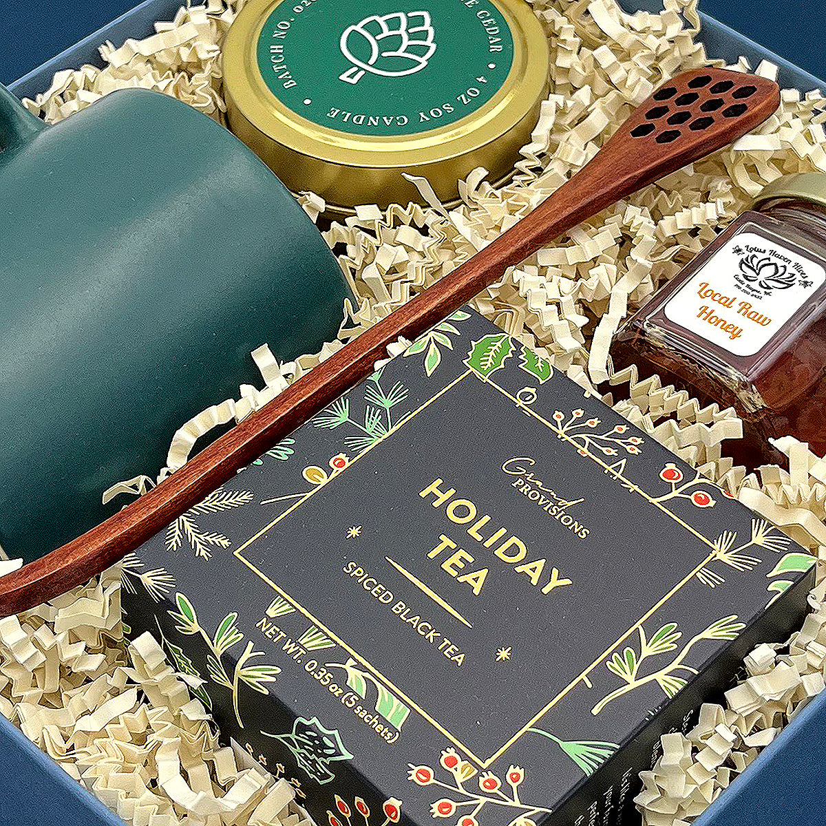 Close up of gift set with holiday tea, honey, balsam candle and green ceramic mug.