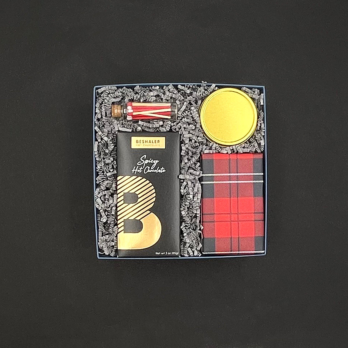 Gift set with spicy hot chocolate, ginger snap cookies, snow and pine candle and peppermint stick matches on a dark background