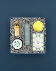 Thoughty Welcome Relief wellness gift box with Thistle Farms essential oil roll-on, French pear soap, eucalyptus mint body butter, gold matches in a corked vial, and a eucalyptus jasmine candle, nestled in gray crinkle paper against a deep navy background.