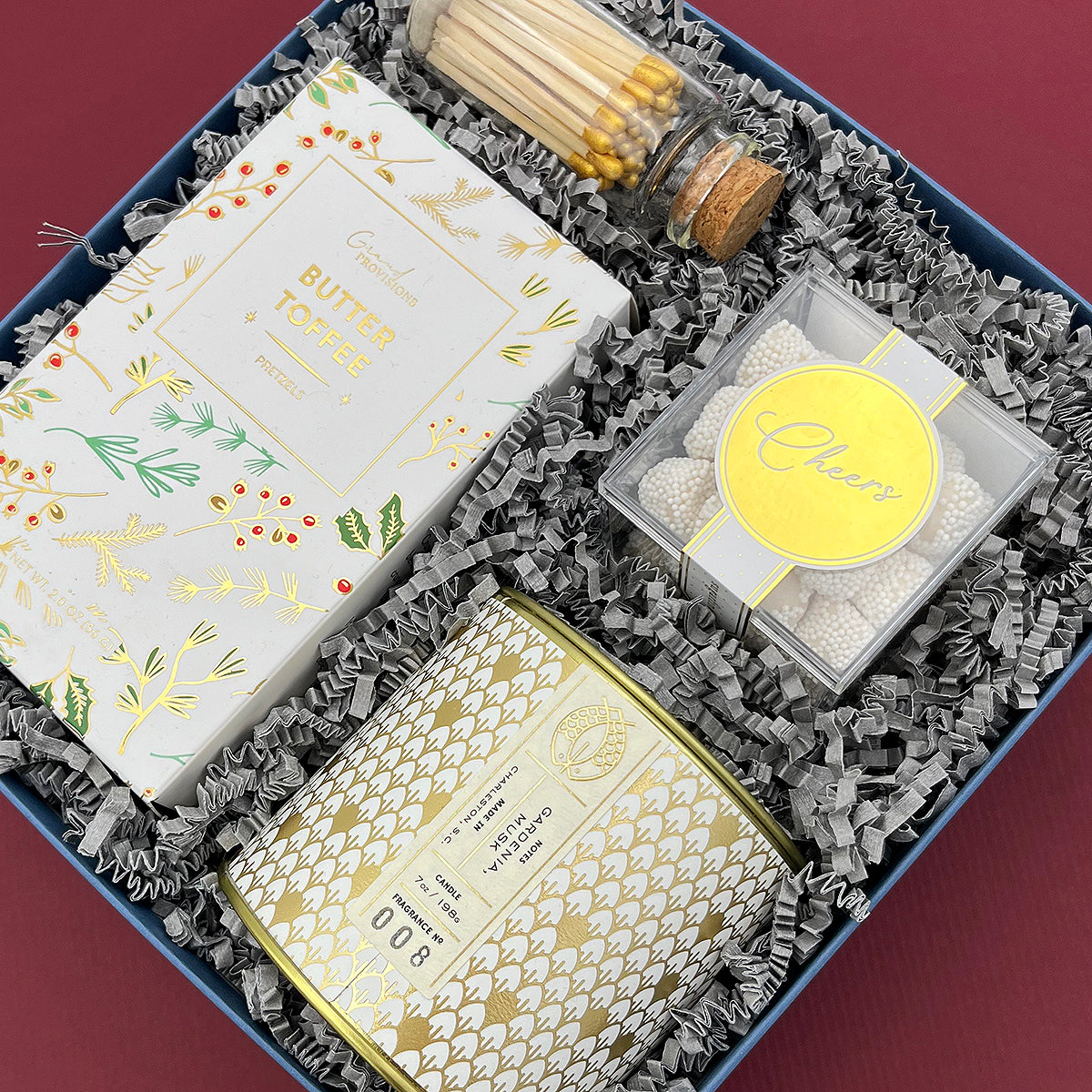 Winter White Gift Box featuring Candlefish candle, gold matches, and holiday snacks.