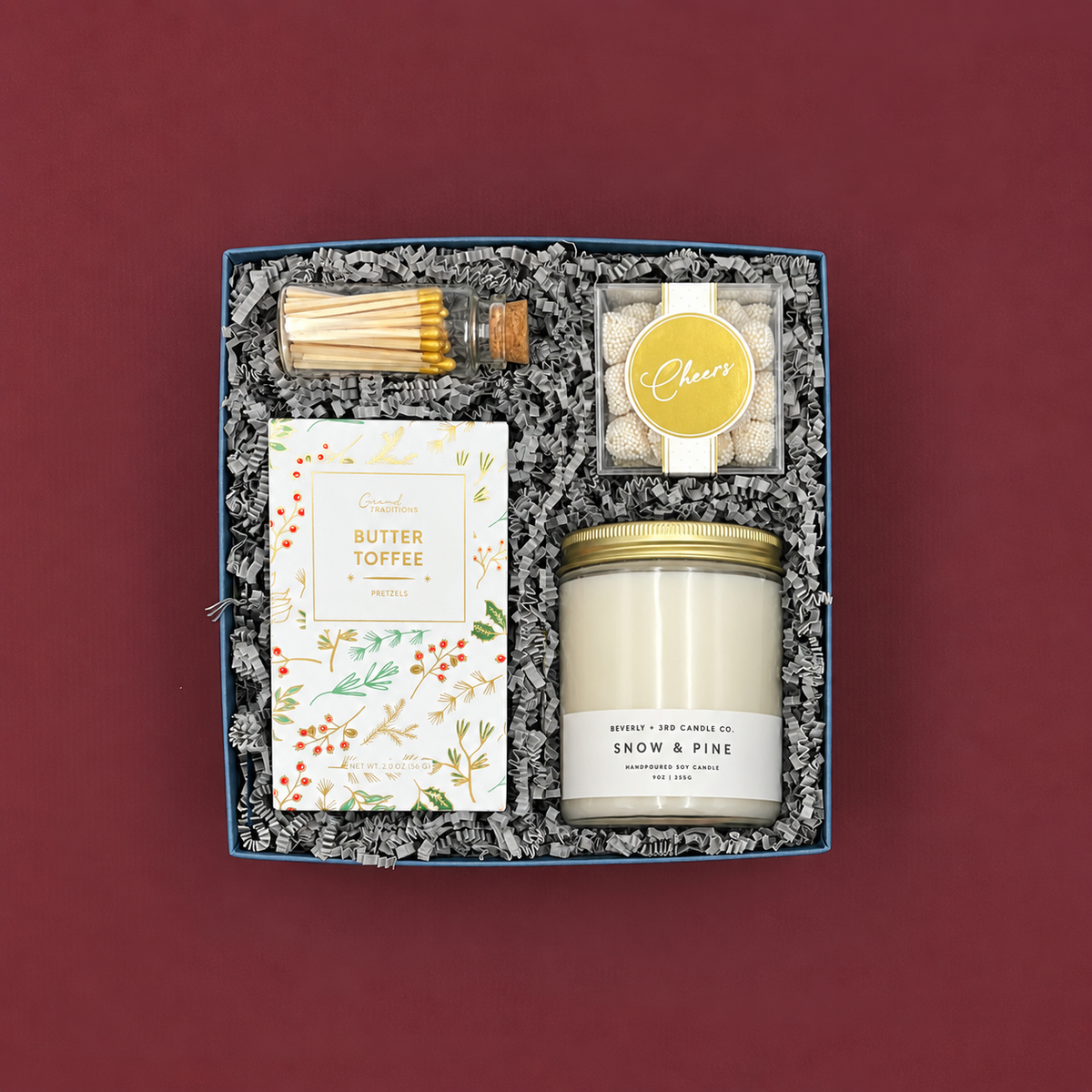 Elegant winter holiday gift with pine candle, gold-tipped matches, sweet and salty pretzels, and champagne-inspired candy.