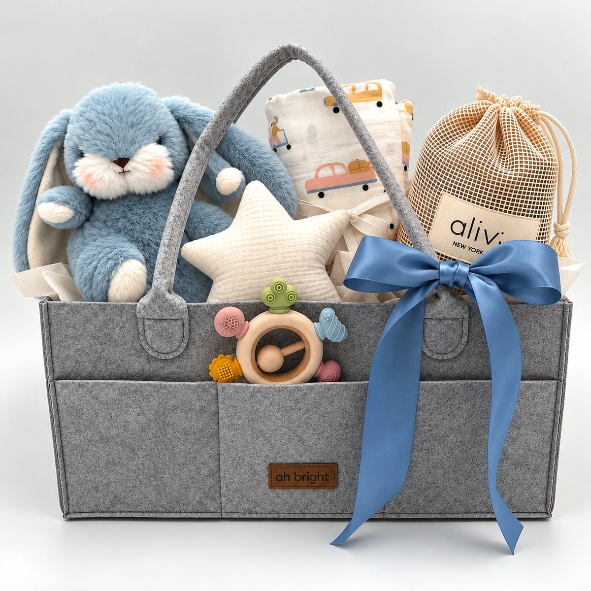 Gray diaper tote with blue ribbon, plush toy, and baby swaddle, and teether rattle on a white background